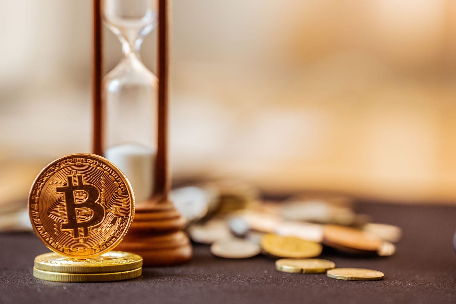 Gold bitcoin coin standing beside a brass hourglass with small coins scattered on a table